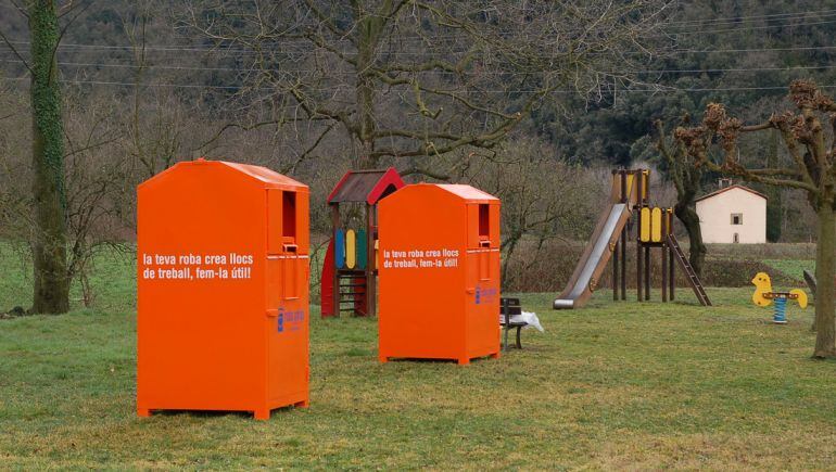Dos contenidors taronja de recollida de roba a prop d&#039;un parc infantil.