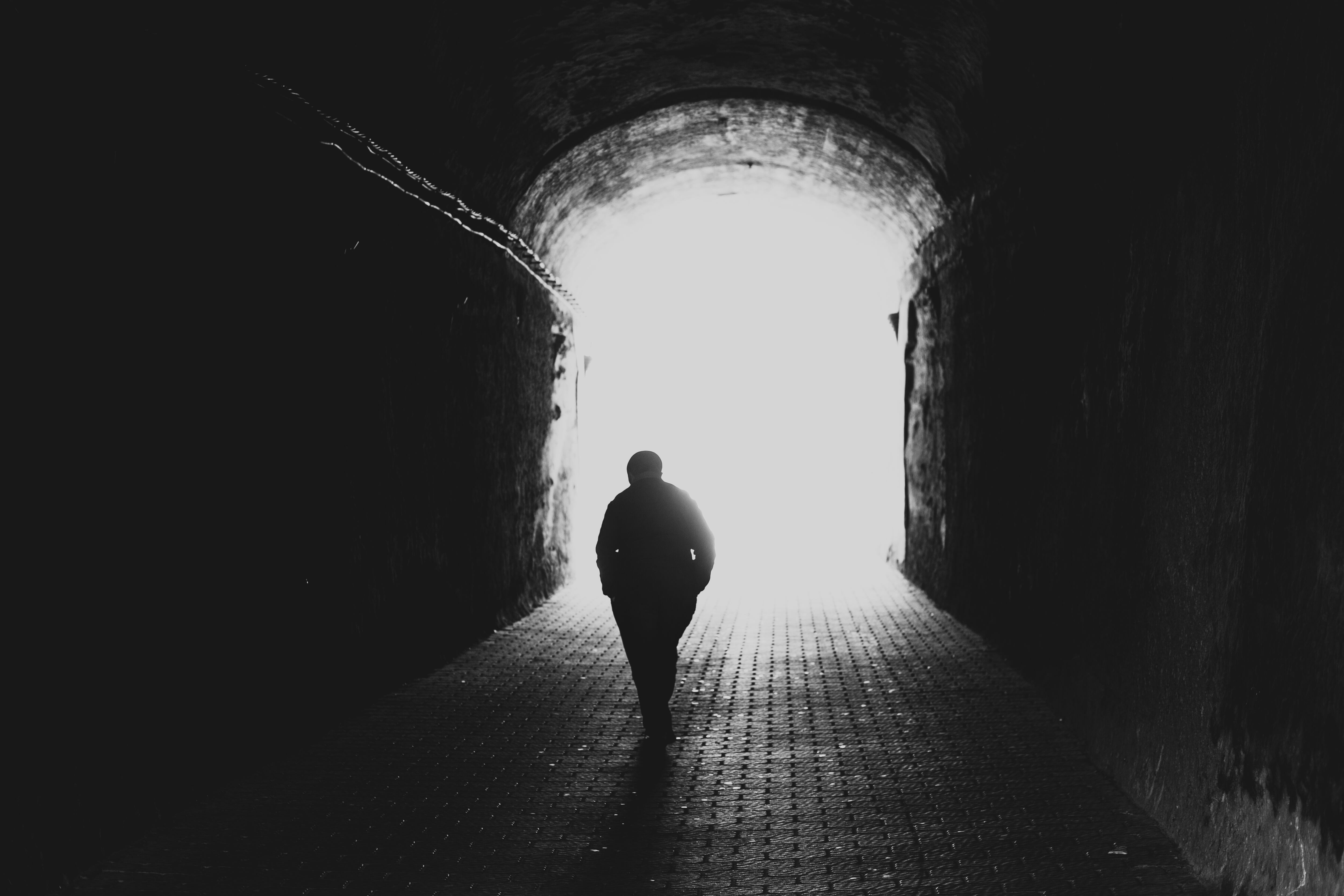 Rear view silhouette of a senior man walking towards the light at the end of the tunnel