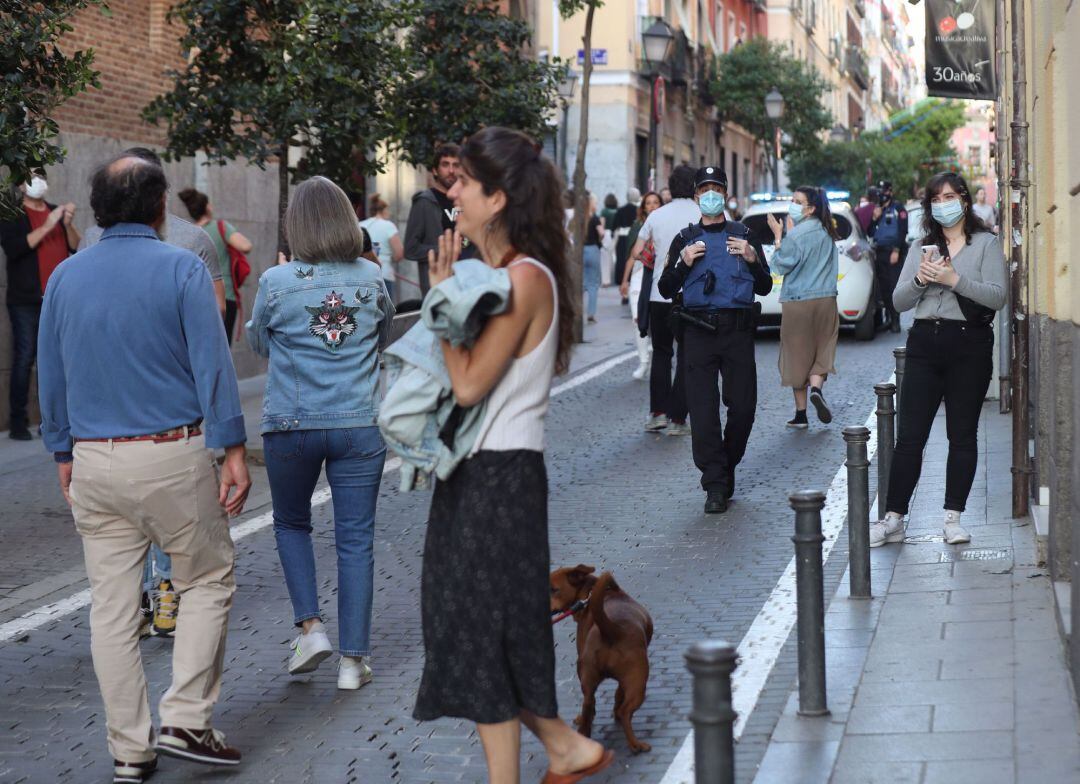 Gente pasea este sábado en una calle del barrio de Malasaña de la capital mientras patrulla la policía local.