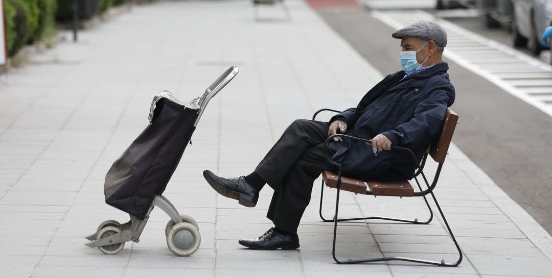 Un hombre de edad avanzada espera en un banco protegido con mascarilla