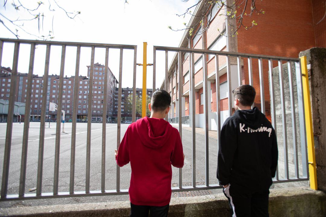 Dos adolescentes observan el patio cerrado de un colegio durante el confinamiento por el estado de alarma, cuando España es el único país que no deja a los menores salir a la calle y un día después de que la ministra de Educación anunciara que el curso escolar acabará en junio y que permitirá a las autonomías abrir los colegios en julio para dar clases voluntarias de refuerzo. 