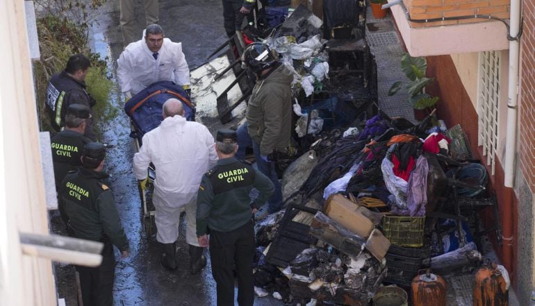 Efectivos de los servicios funerarios trasladan el cuerpo de uno de los tres fallecidos en el incendio