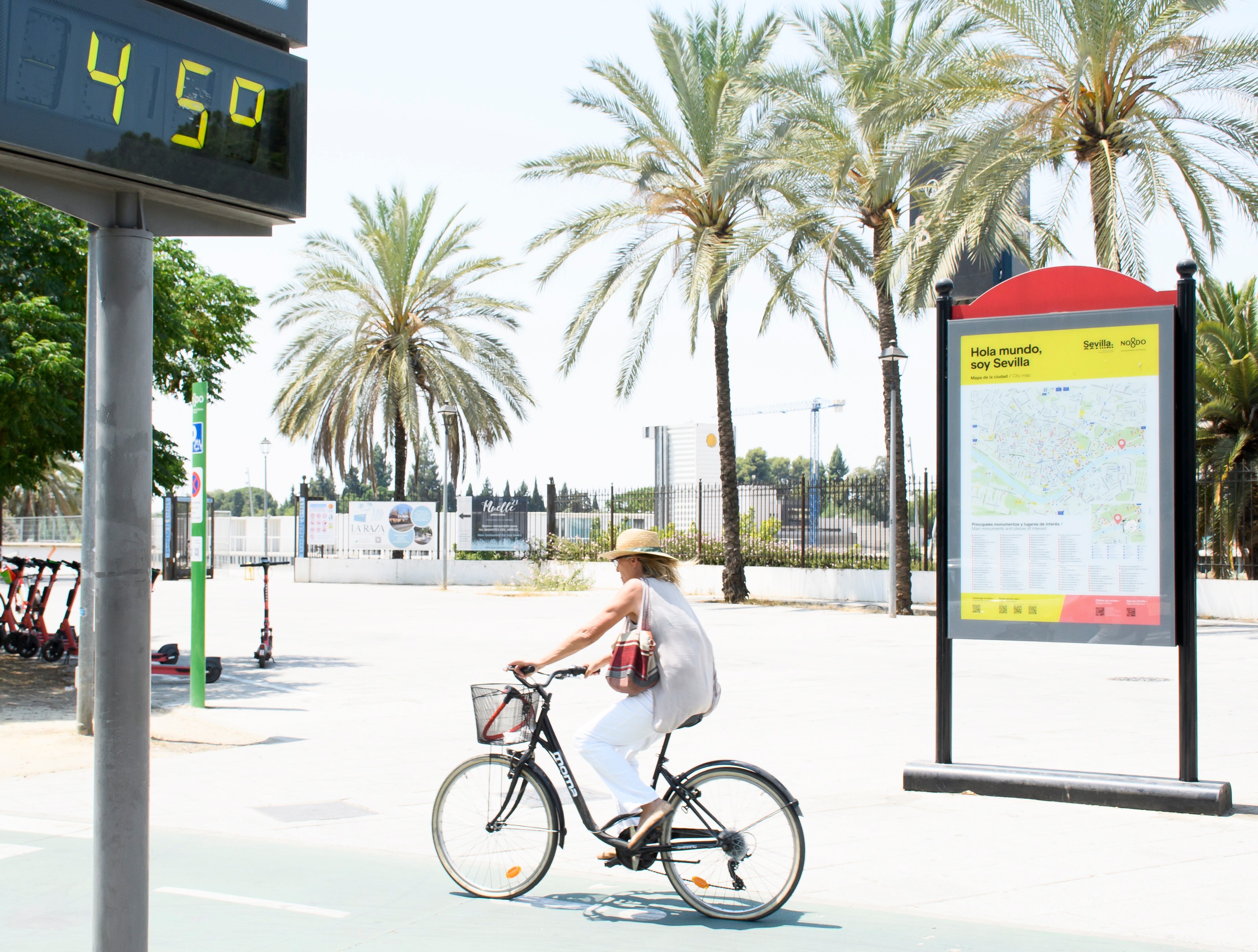 GRAFAND1654. SEVILLA, 15/07/2022.- Una mujer en bicicleta pasa junto a un termómetro de calle en Sevilla que marca 45 grados, hoy viernes cuando continúa la ola de calor aunque con una ligera bajada, con temperaturas que alcanzarán los 43 grados en Sevilla y Córdoba, y avisos naranja en las provincias de Jaén y Huelva, según el pronóstico de la Agencia Estatal de Meteorología (Aemet). EFE/ Raúl Caro.