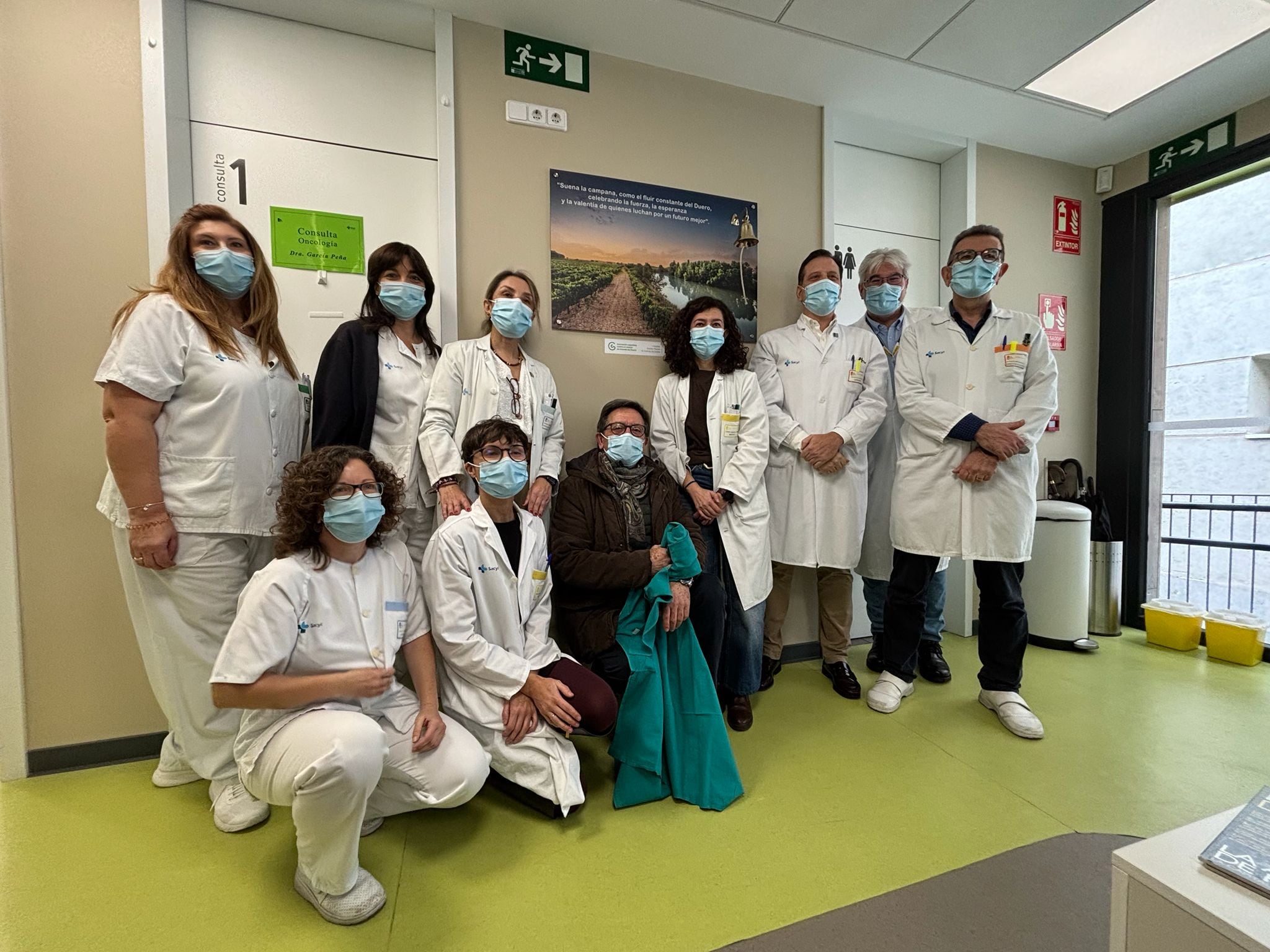 Antonio de las Heras, presidente de la AECC Aranda (de verde), con el personal sanitario del Hospital de Día Oncohematológico, posando junto a la campana