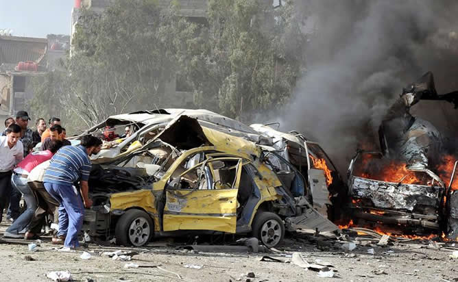 Hombres sirios empujan los restos de un coche destrozado como consecuencia del doble atentado perpetrado en la zona de Qazaz, a unos cinco kilómetros al sur de Damasco