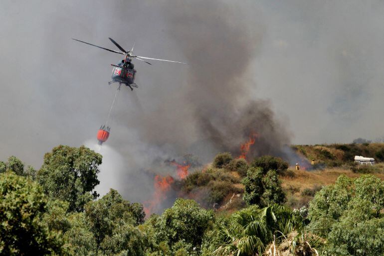 Un helicóptero echa agua en un incendio forestal que se ha  registrado en la provincia de Cádiz y que ha obligado a desalojar varias viviendas.