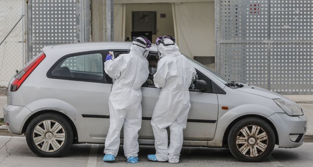 Dos sanitarios realizan una prueba PCR a una persona desde su vehículo