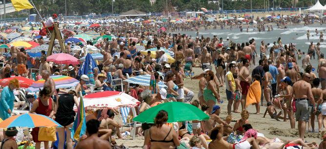 Decenas de turistas disfrutan del agua y la arena en la playa levantina del Postiguet, en Alicante.