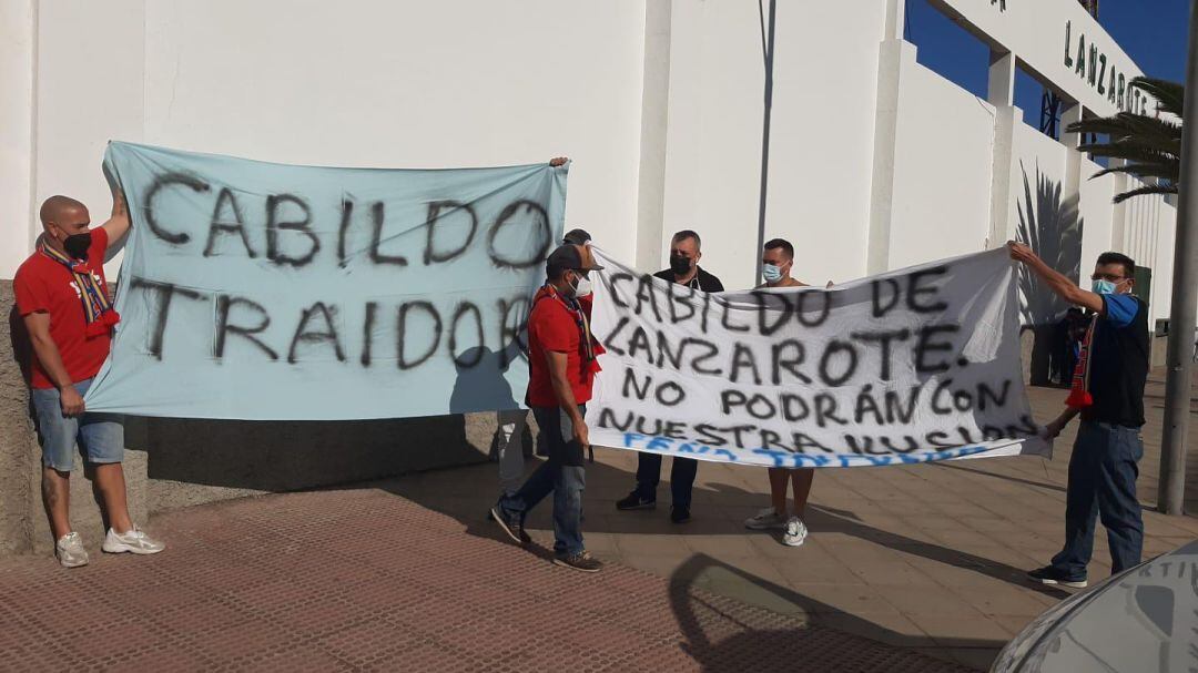 Con pancartas en las que se lee &quot;Cabildo traidor&quot; la Peña Trifulka, Amarillos Lanzarote y personal de otros clubes se concentran frente a la Ciudad Deportiva durante el encuentro con la UD Guía.