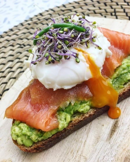 Salmón, fuente de vitamina D, acompañado de aguacate, huevo, germinados y salicorinia, todo sobre pan integral