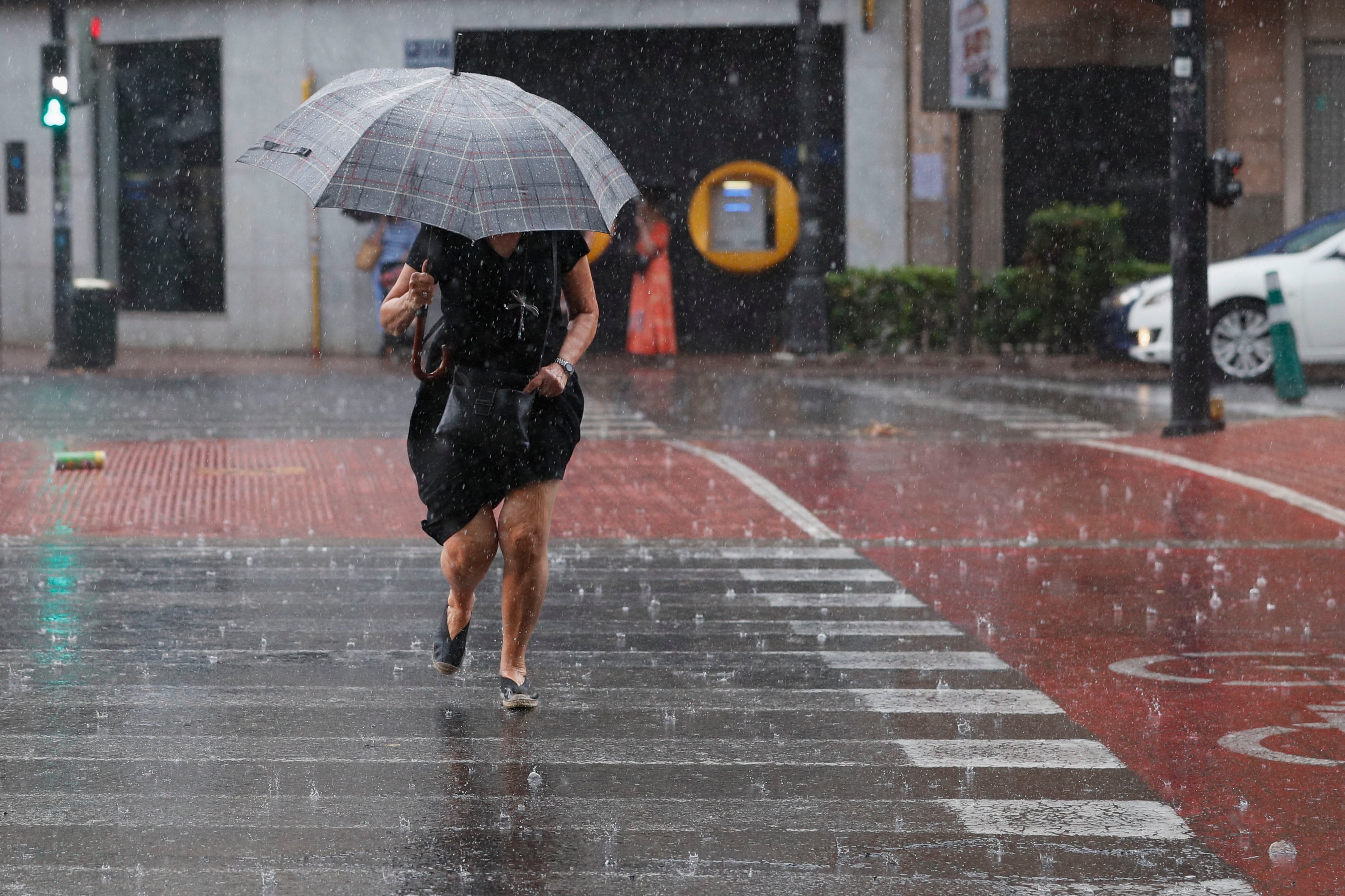 Una mujer camina por un paso de peatones bajo una intensa lluvia en Valencia. EFE/ Juan Carlos Cárdenas