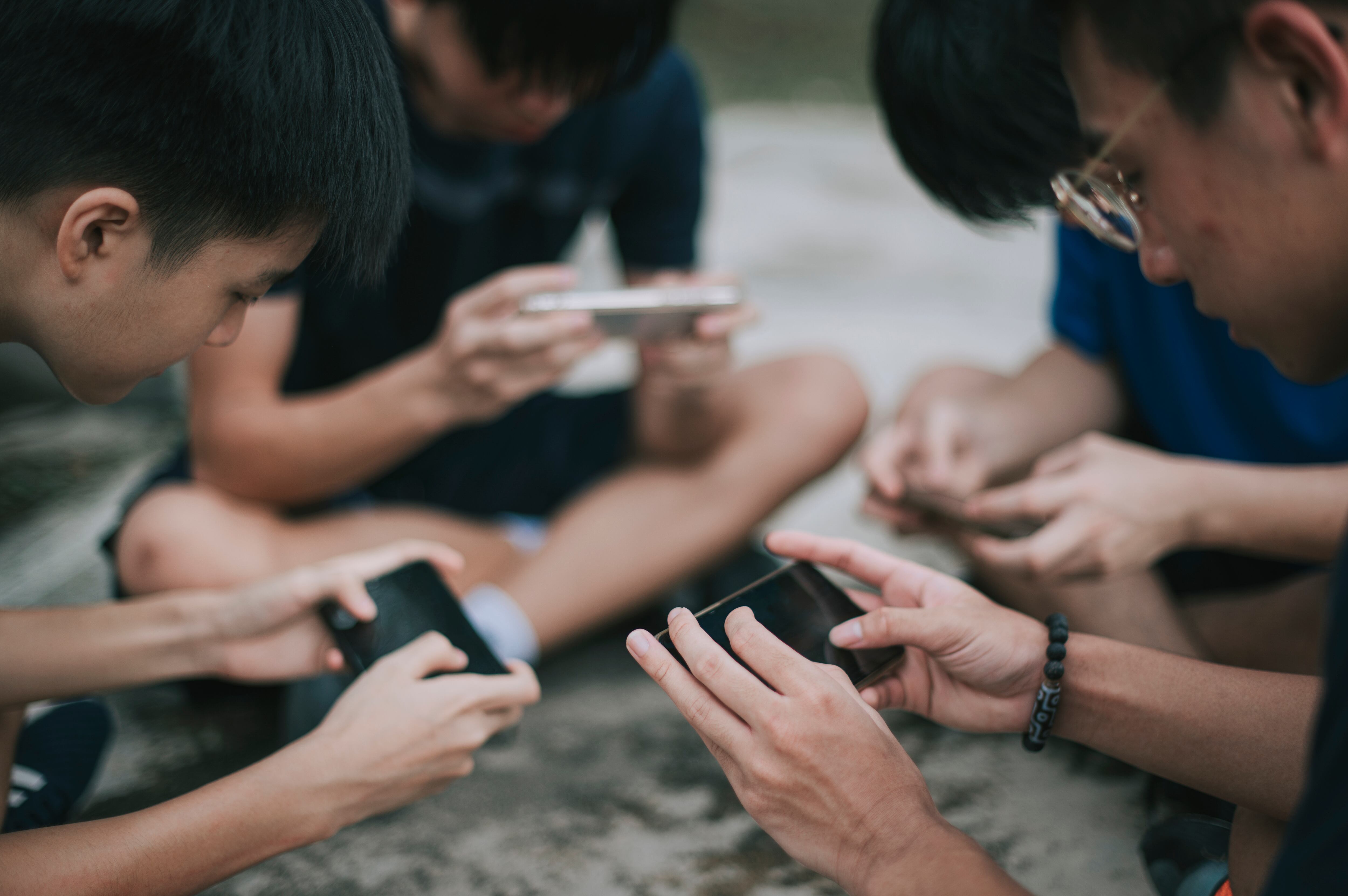 an asian chinese group of teenage boys playing mobile game in the basketball court after school using phone