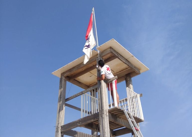 Un operario de Criz Roja iza la bandera roja en la playa de El Saler junto a la bandera blanca avisando del avistamiento de medusas