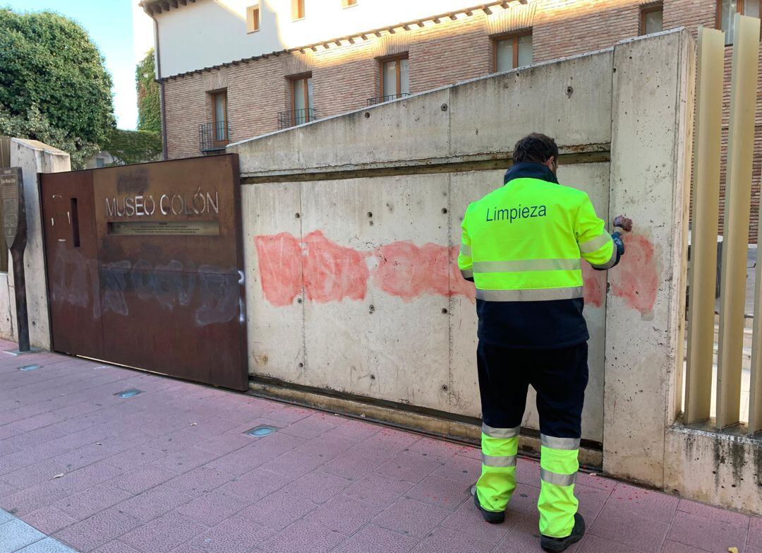 Operario del Servicio de Limpieza intenta retirar la pintada en la Casa Colón