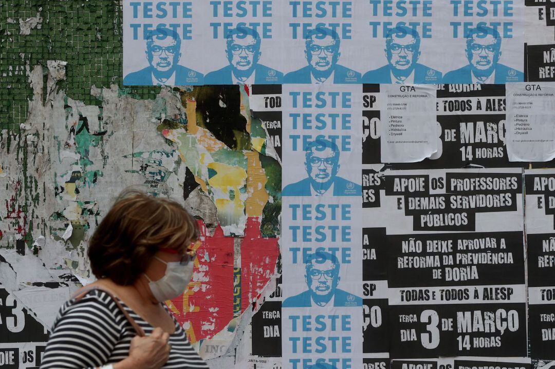 Una mujer pasa frente a carteles con la imagen del director general de la Organización Mundial de la Salud (OMS), Tedros Adhanom, este lunes en una calle del centro de la ciudad de Sao Paulo (Brasil)