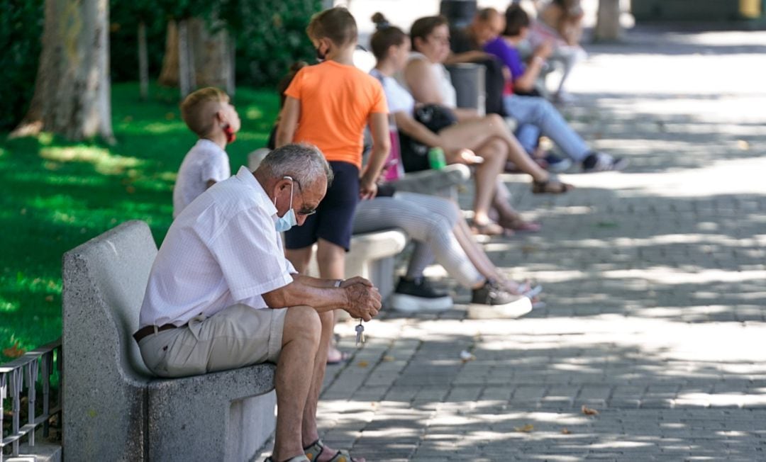Un anciano con mascarilla sentado en un banco.