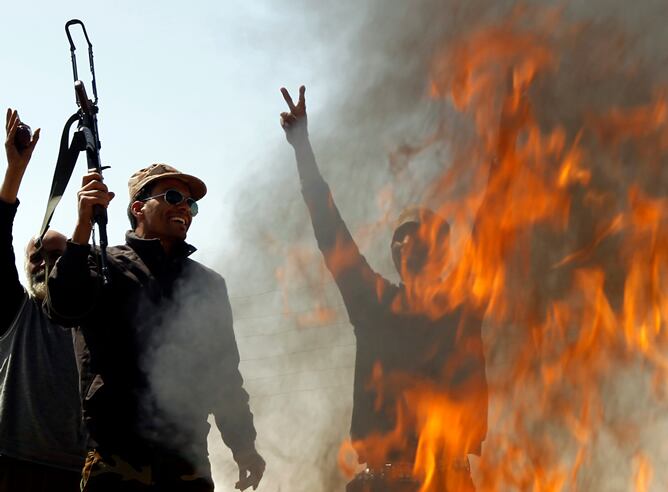 Combatientes rebeldes junto a un fuego encendido para quemar la ropa de los soldados leales al líder libio Muammar Gaddafi en una calle cerca de Bengasi-Ajdabiyah