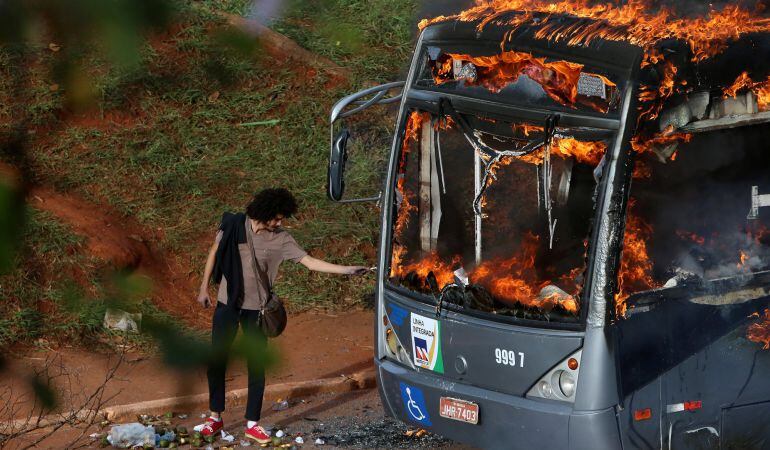 Un hombre se enciende un cigarrillo con las llamas de un autobús quemado por manifestantes contrarios al gobierno de Brasil.