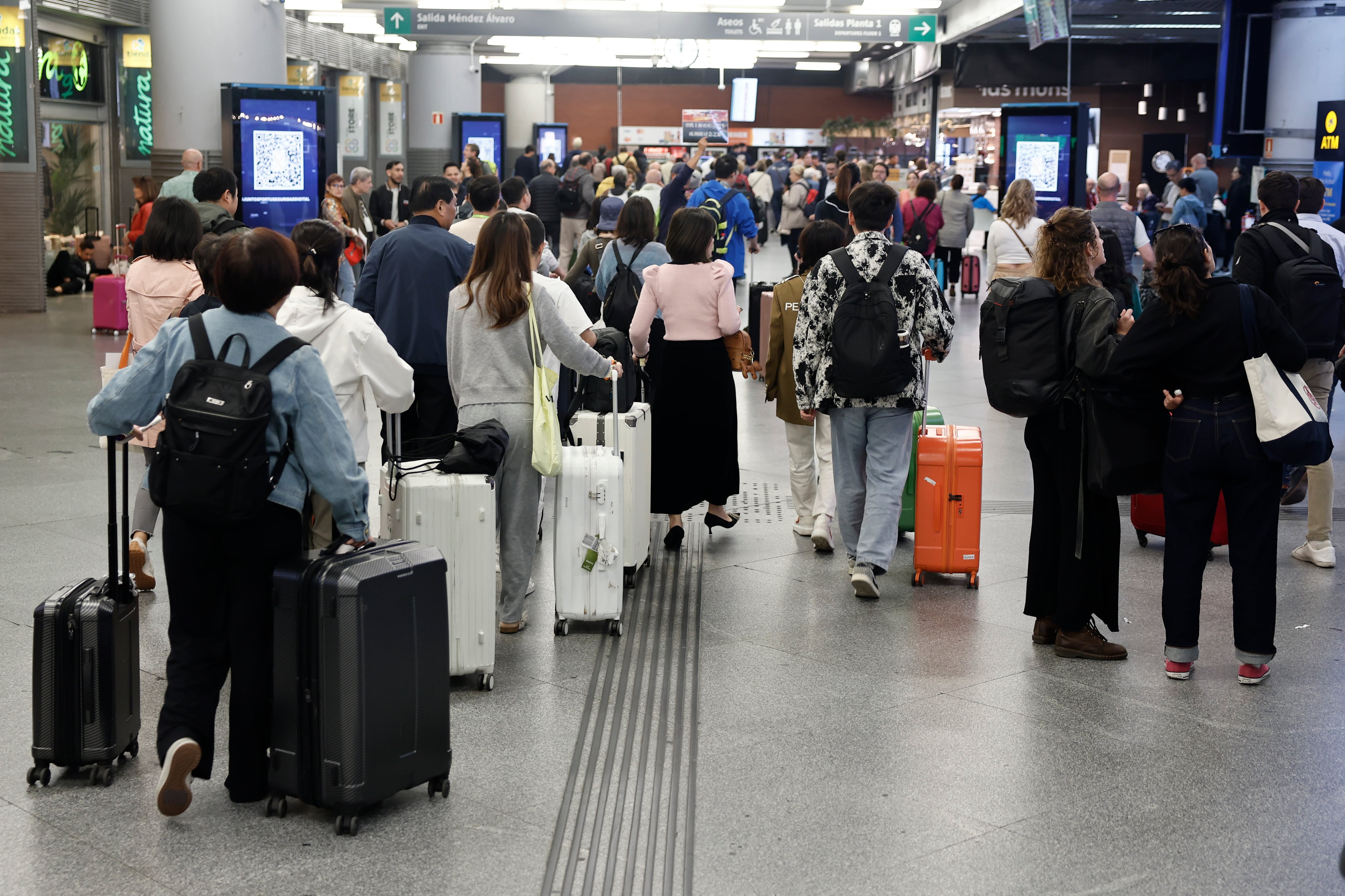 Varias personas esperan la salida de su tren en la estación de Atocha en Madrid este domingo.