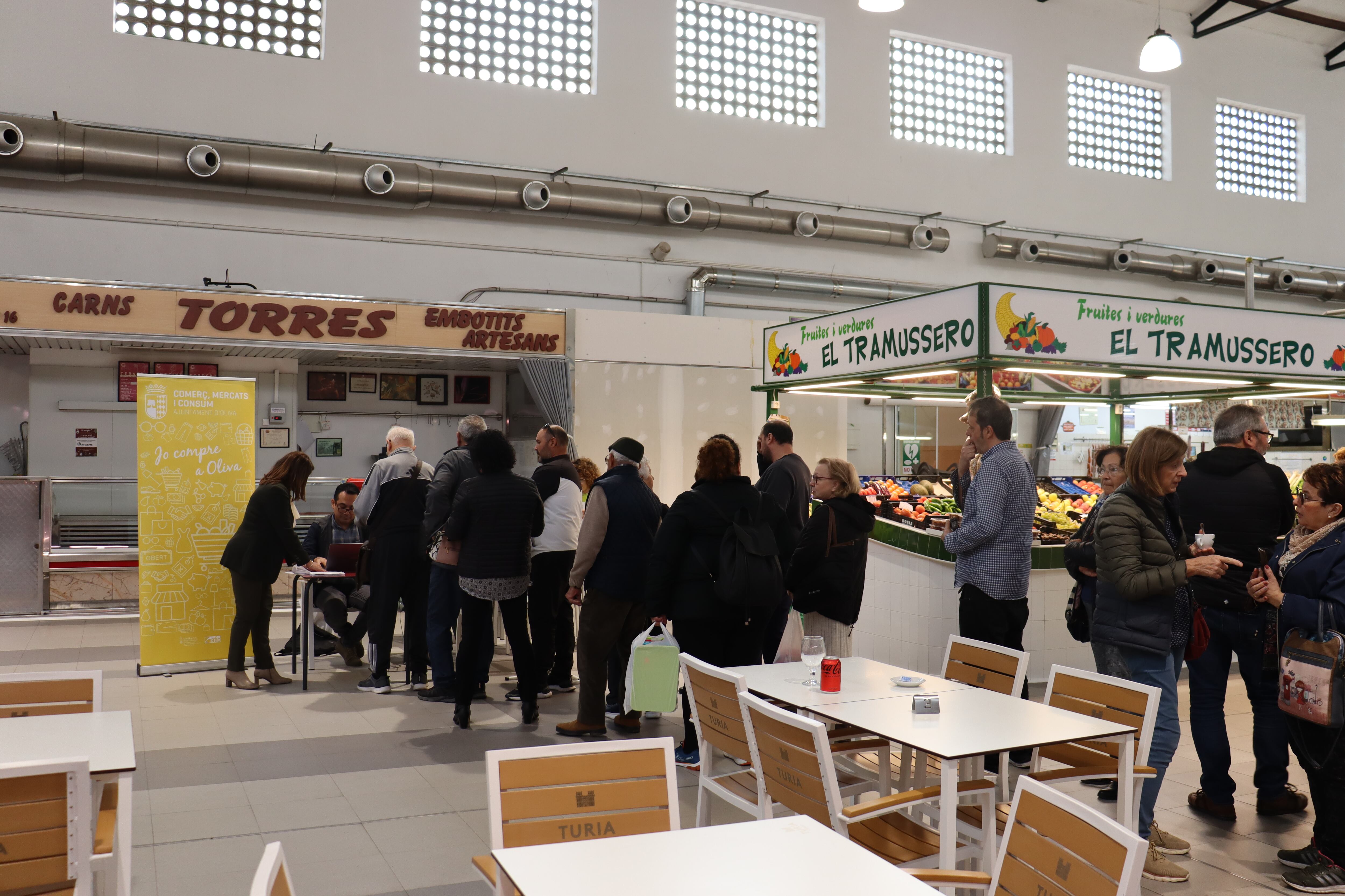 Vecinos y vecinas de Gandia hacen cola para recoger sus bonos descuentos en el Mercado Municipal.