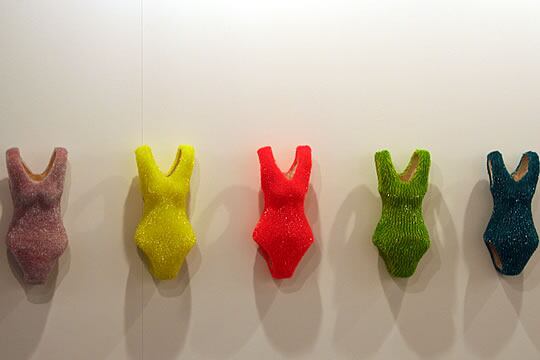 Instalación coreana en la cual se aprecian varios bañadores de cartón recubiertos de escamas de plástico transparente de diferentes y llamativos colores.