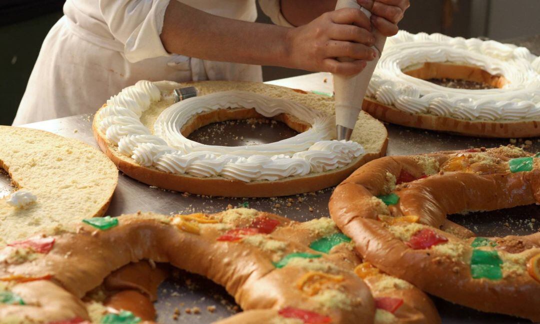 Un pastelero rellenando de nata uno de los roscones solidarios