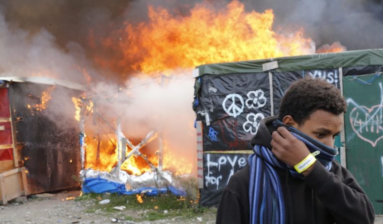 Un migrante se protege el rostro al pasar junto a chabolas en llamas durante el desmantelamiento del campamento de Calais (Francia).