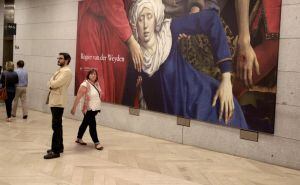 Dos espectadores junto a un cartel con un fragmento del &quot;Descendimiento de la cruz&quot; del flamenco Rogier van der Weyden, en el museo de El Prado.