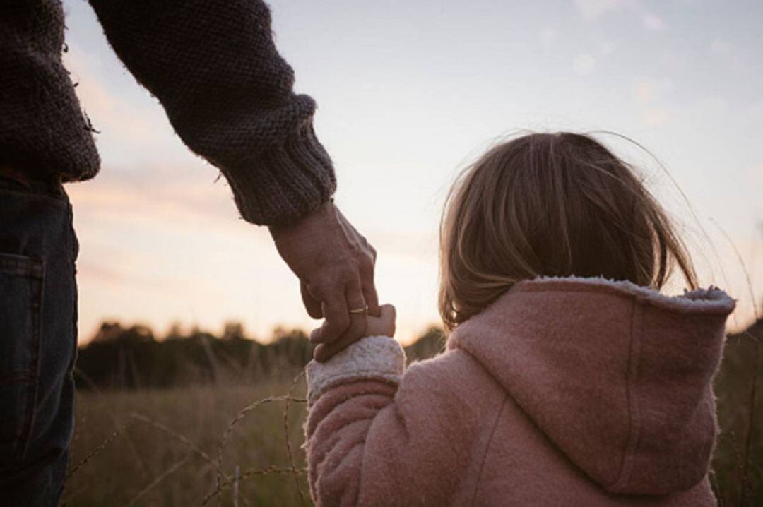 Una niña sostiene la mano de un adulto