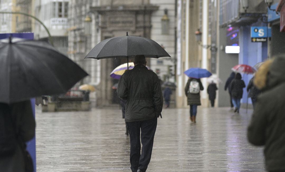 Transeúntes caminan protegidos por una vía de A Coruña, Galicia.