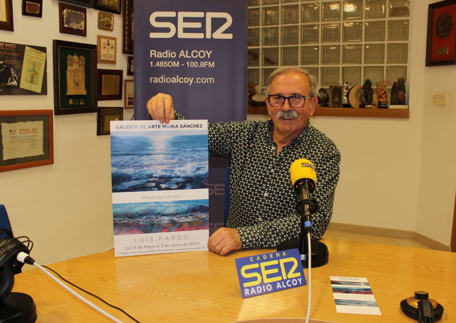 Luis Pardo, en el estudio de Radio Alcoy, muestra el cartel de la exposición