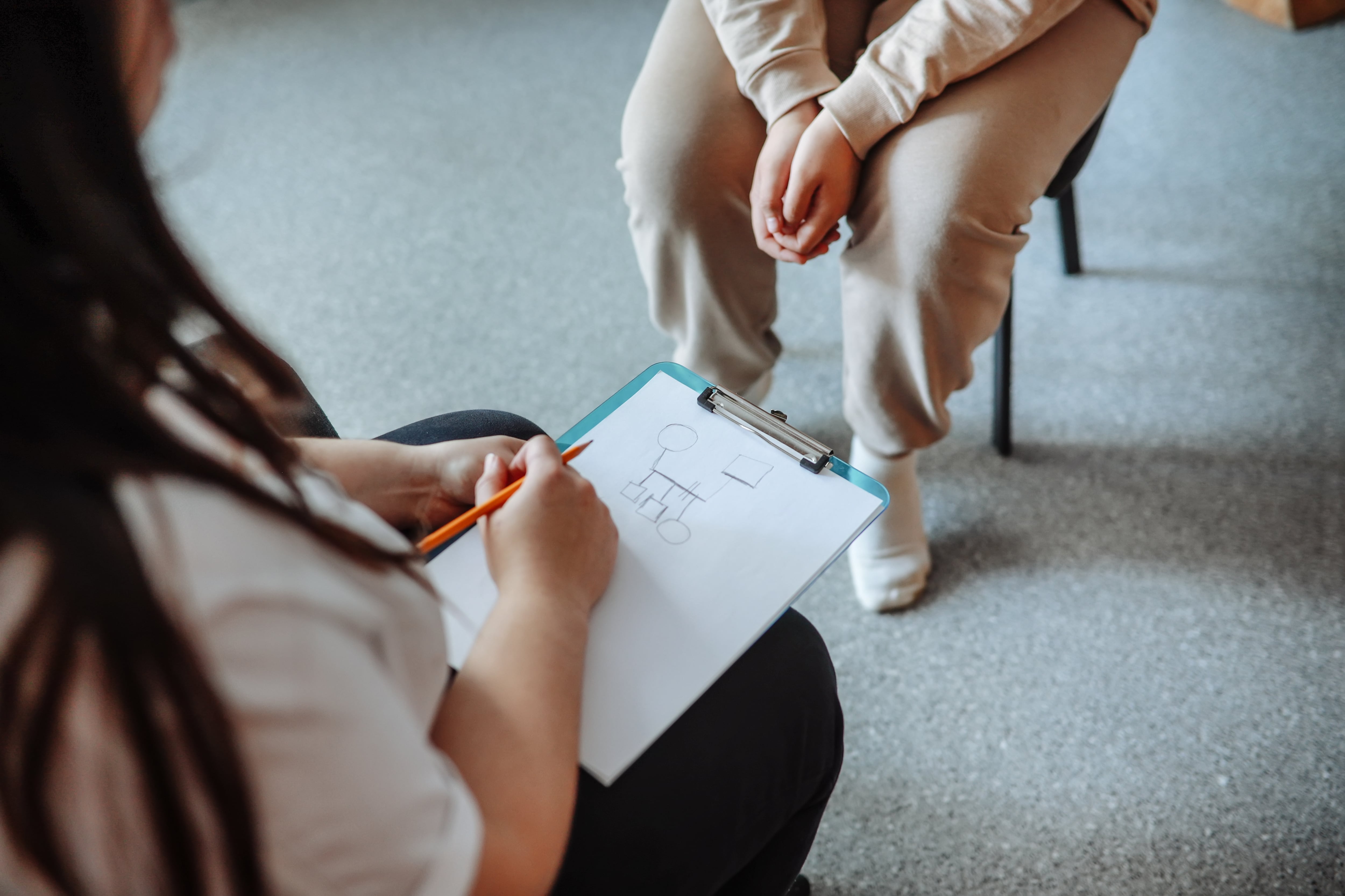 Psychologist makes genogram on clipboard while counseling teenage girl.