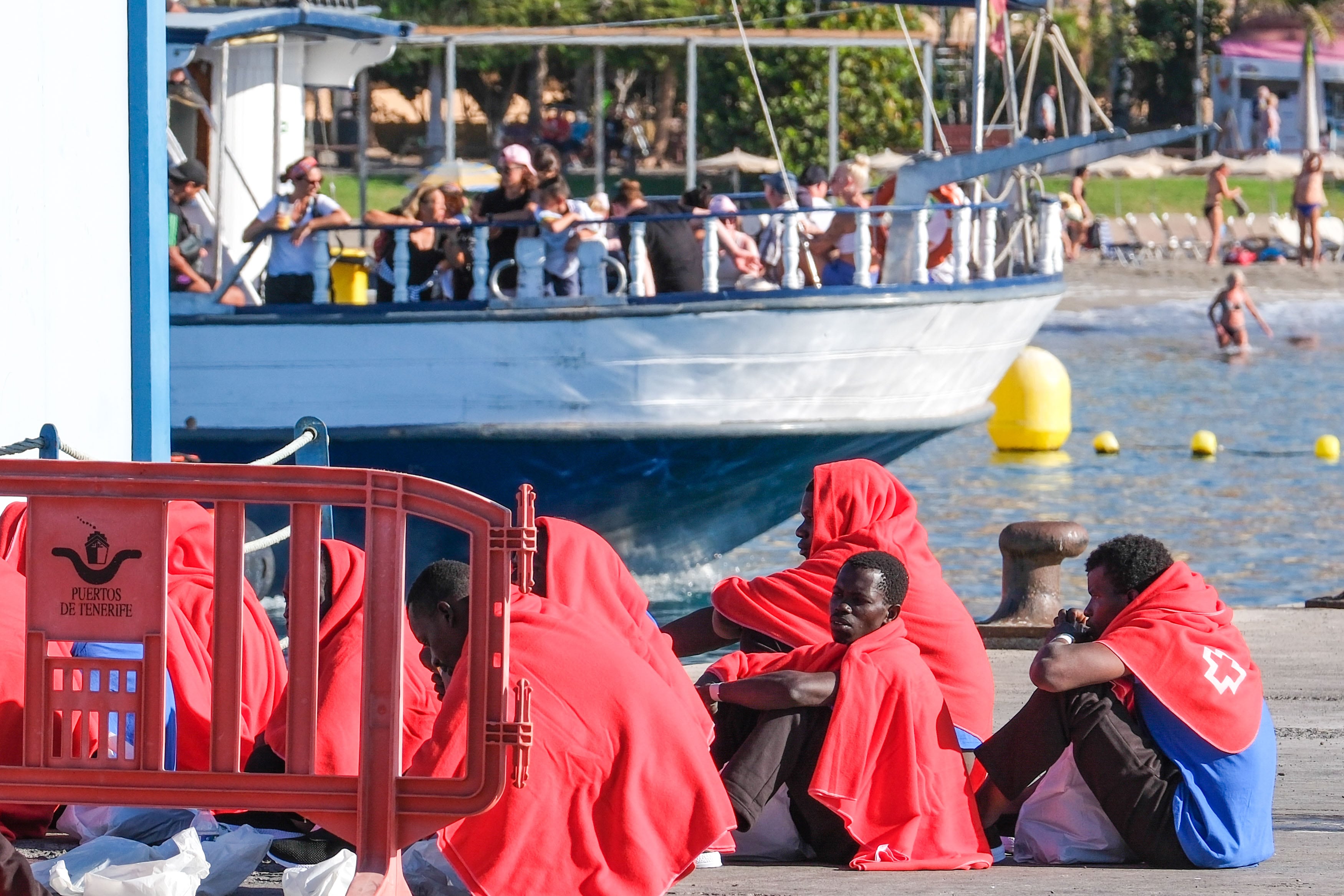 LOS CRISTIANOS (TENERIFE), 26/10/2023.- Salvamento Marítimo ha escoltado este jueves a un cayuco con 23 migrantes de origen subsahariano a bordo, entre ellos dos menores, hasta el puerto de Los Cristianos, en Tenerife. En la imagen, un barco de ocio turístico arriba el muelle mientras los inmigrantes están siendo atendidos por personal de Cruz Roja y del Servicio Canario de Salud.EFE/ Alberto Valdés
