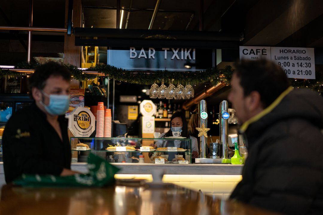 Dos clientes conversan mientras una camarera sirve platos de comida en un establecimiento de Vitoria 