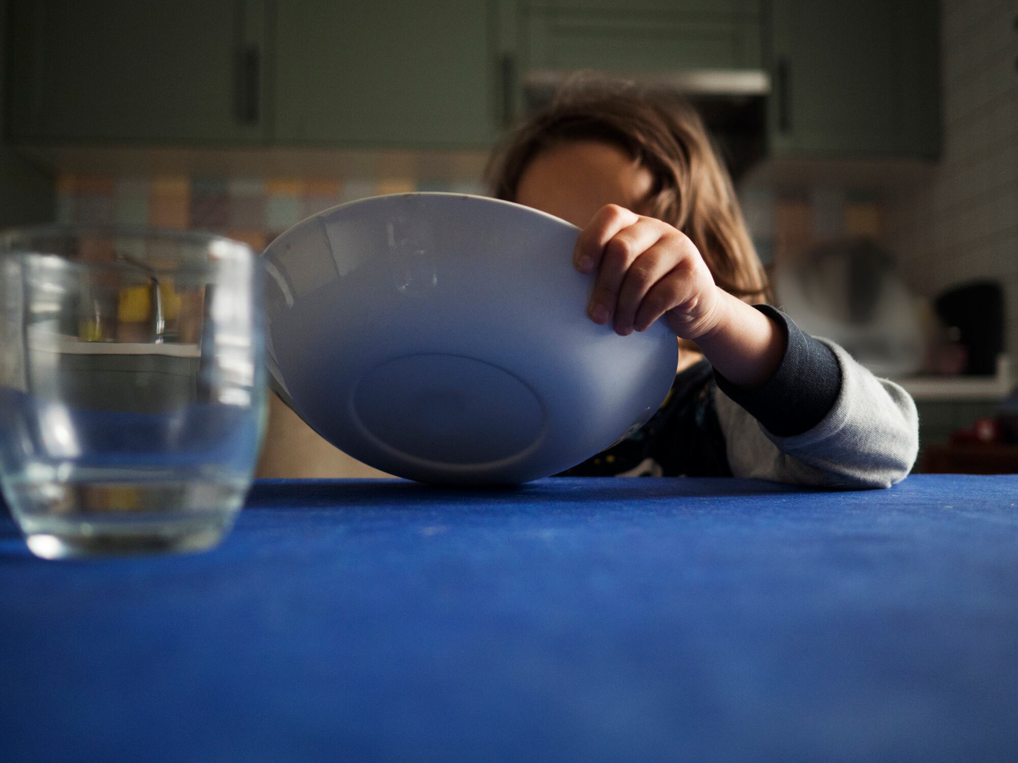 Una niña comiendo de un plato en una mesa donde también hay un vaso de agua