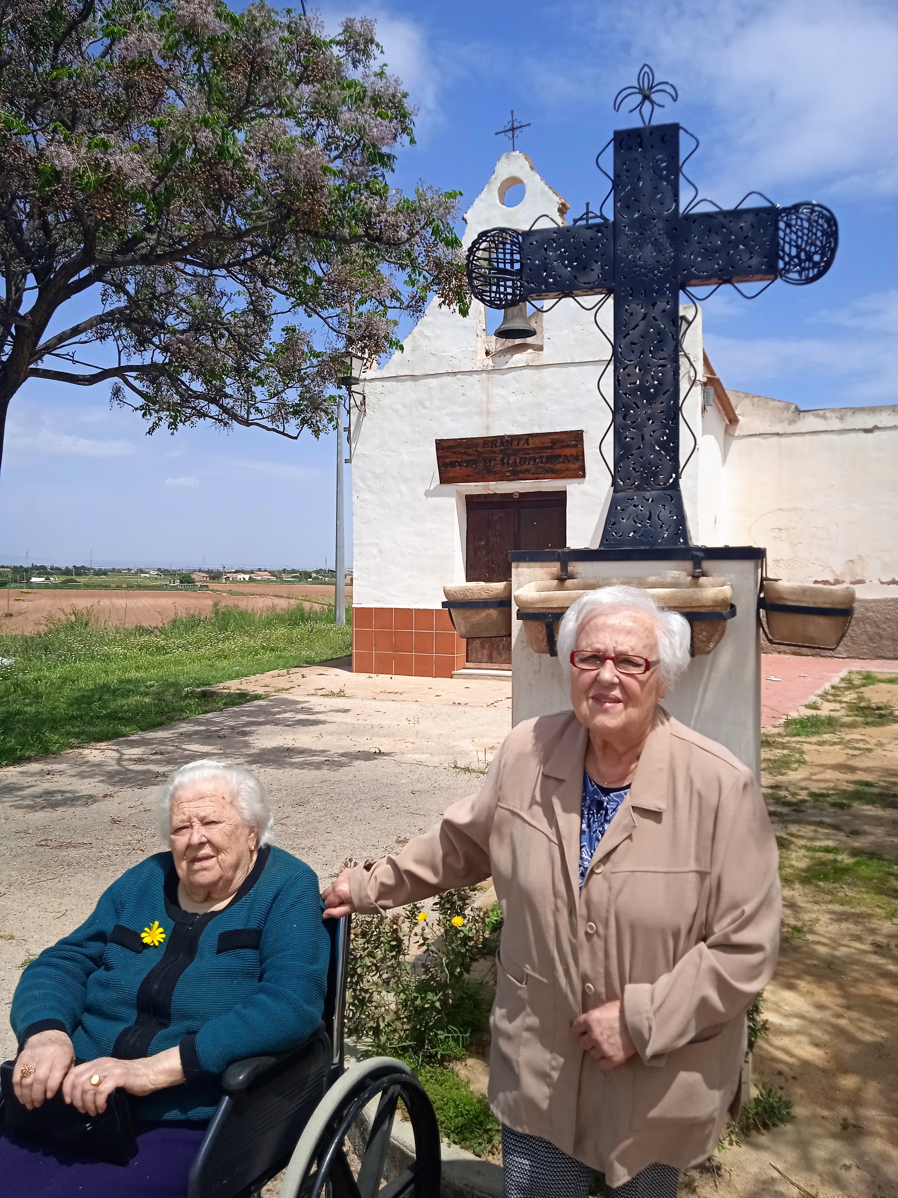 Cari y La Nena con 77 y 84 años, junto a la cruz de hierro para celebrar Los Mayos, obra del escultor Alhameño Alfonso Núñez, que el año pasado se recuperó para sustituir a la antigua cruz desaparecida en el exterior de la ermita de La Magdalena. Año 2022