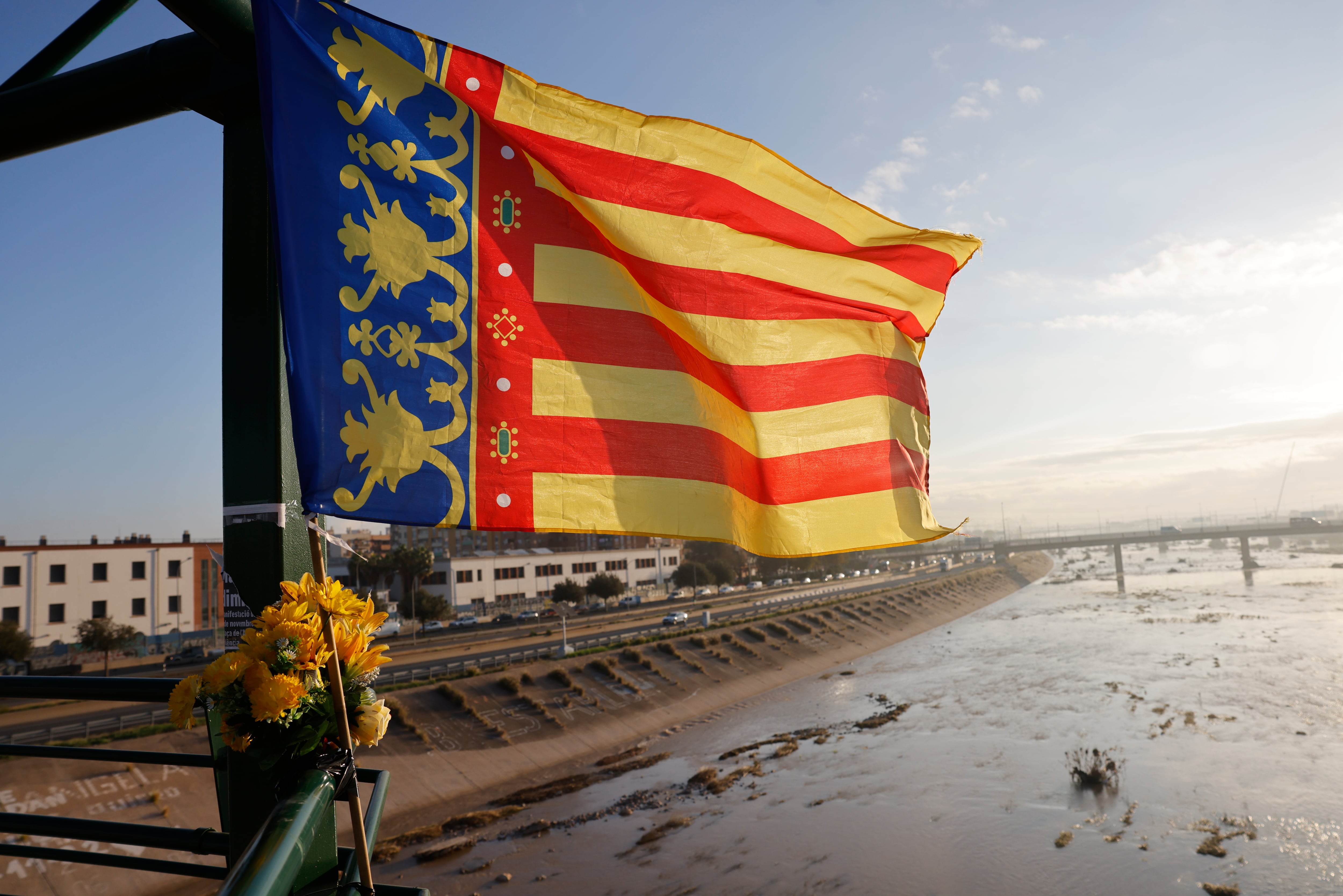 VALENCIA, 07/11/2024.- Una bandera de la Comunidad Valenciana junto a un ramillete de flores cuelga de la pasarela que va de Valencia hacia La Torre, este jueves. Voluntarios, fuerzas de seguridad, bomberos, militares y vecinos de las localidades más afectadas por la dana continúan con las tareas de limpieza mientras los equipos de rescate siguen rastreando la zona para intentar localizar a las personas que aún sigue desaparecidas. EFE/Ana Escobar
