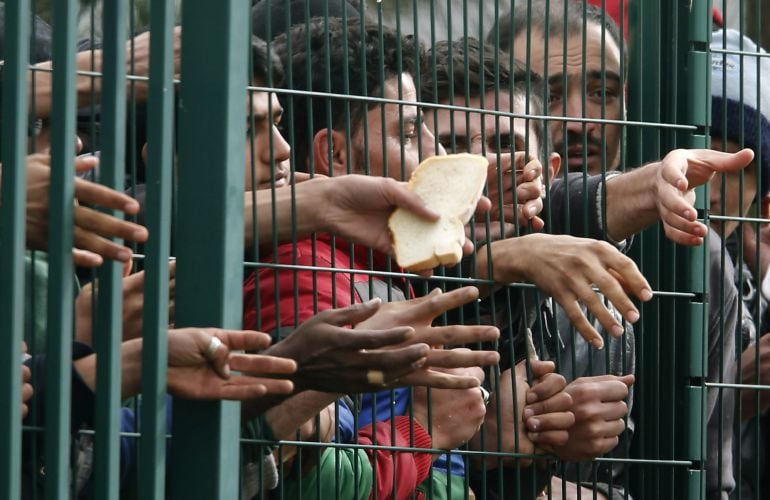 Refugiados piden comida a trabajadores de la Cruz Roja tras una valla en el campo de refugiados en Brexice (Eslovenia).