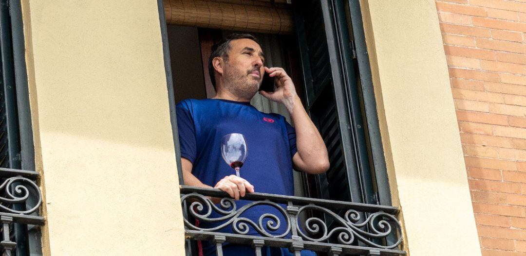 Un vecino asomado al balcón de su casa con una copa de vino