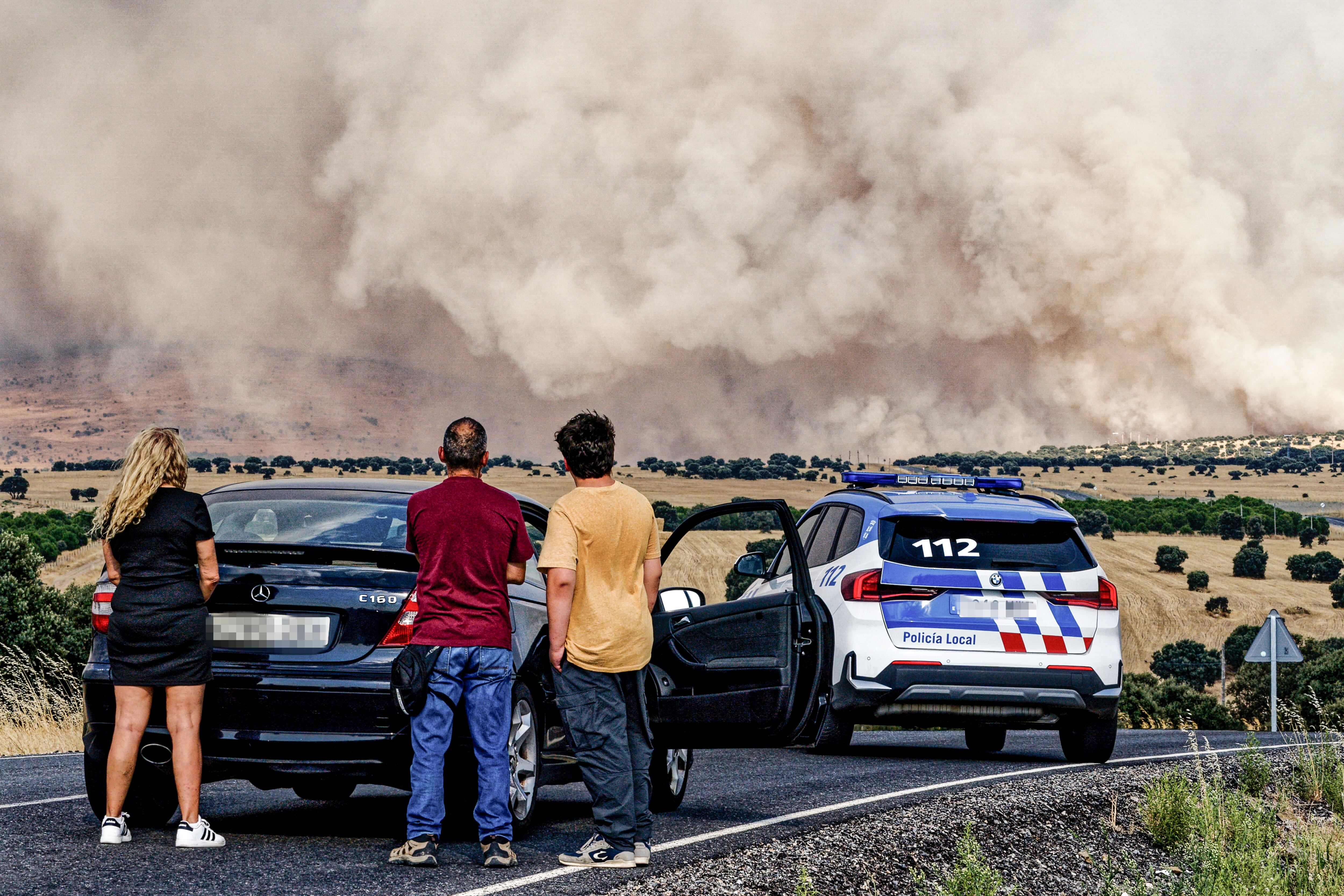 Un grupo de personas paradas en la carretera AV-500, la cual se encuentra cortada en las proximidades de Urraca-Miguel, barrio anexionado de Ávila capital con motivo del incendio que azota la zona.