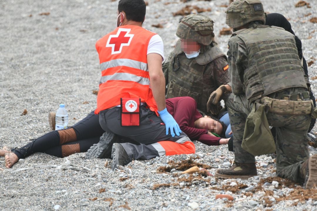 Un trabajador de la Cruz Roja y dos militares ayudan a una migrante que ha llegado a la orilla