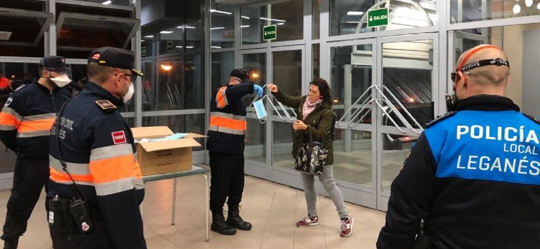 Un miembro de Protección Civil de Leganés entrega una mascarilla a una usuaria del transporte público este lunes por la mañana