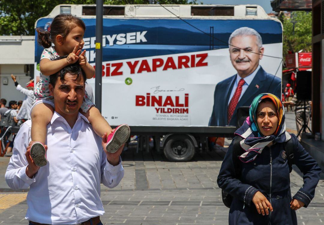 Una pareja con su hija pasan frente a una oficina electoral móvil en la que aparece Binali Yildirim, candidato a la alcaldía de Estambul por el partido gobernante en Turquía, el Partido de la Justicia y el Desarrollo (AKP).