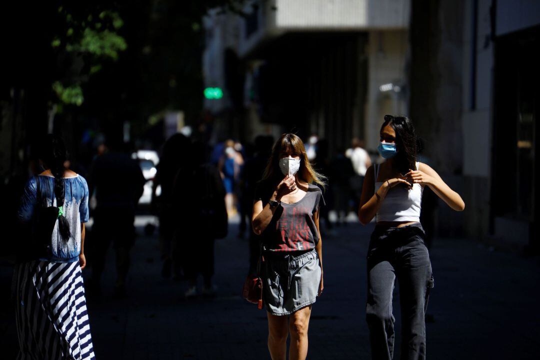 Varias personas caminan por una calle con mascarillas puestas.