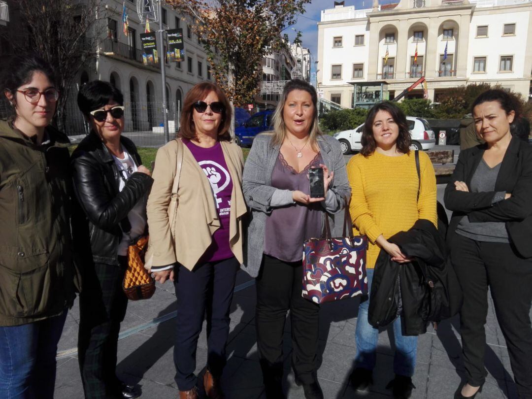 Yolanda Díaz, portavoz adjunta en la plataforma, (c), junto con la portavoz, Alejandra Bou (d), sostiene un móvil, eje de la campaña de este año para conmemorar el Día contra la Violencia de Género.