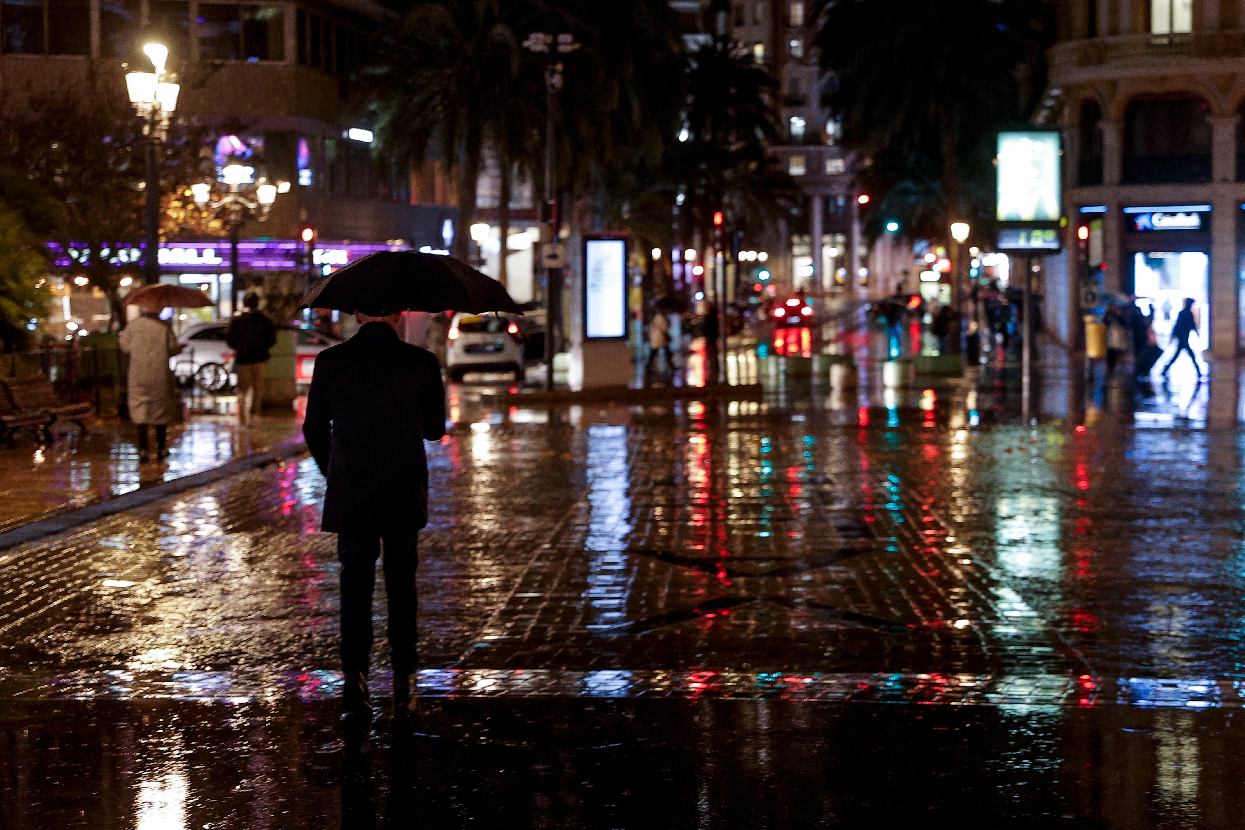 Un hombre camina bajo la lluvia por la plaza del Ayuntamiento de València.