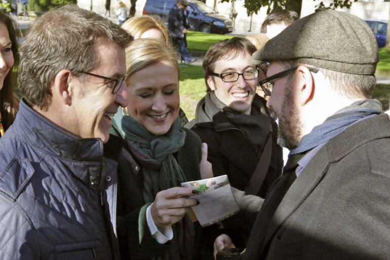 El presidente de la Xunta, Alberto Núñez Feijóo, observa como la presidenta de la Comunidad de Madrid, Cristina Cifuentes, muestra un folleto electoral al alcalde de Santiago, Martiño Noriega