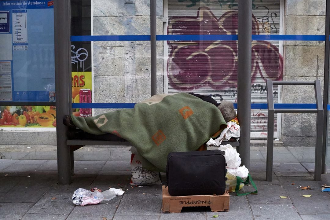 Una persona duerme en una marquesina de autobús en Madrid