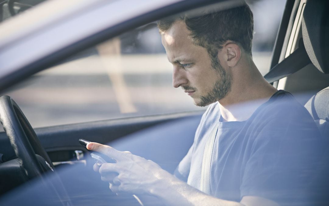 Un hombre consulta el teléfono móvil al volante.