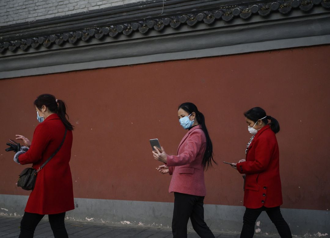 Varias mujeres con mascarilla miran su móvil en las calles de Wuhan tras el levantamiento del confinamiento.